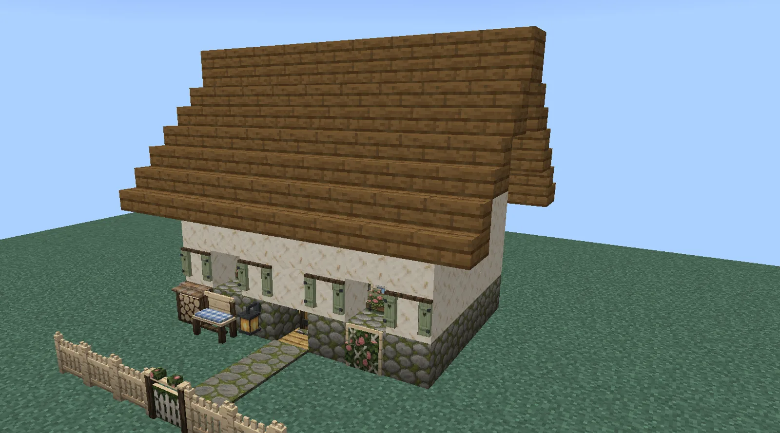 A Minecraft cottage with cob walls on a mossy stone footing, flower box windows with painted shutters, a rose trellis, a flagstone path and a picket fence